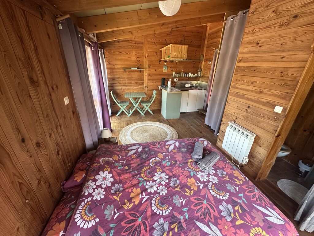 Intérieur du studio de Girolata : lit double, murs et plafond en bois, baie vitrée ouverte sur la terrasse